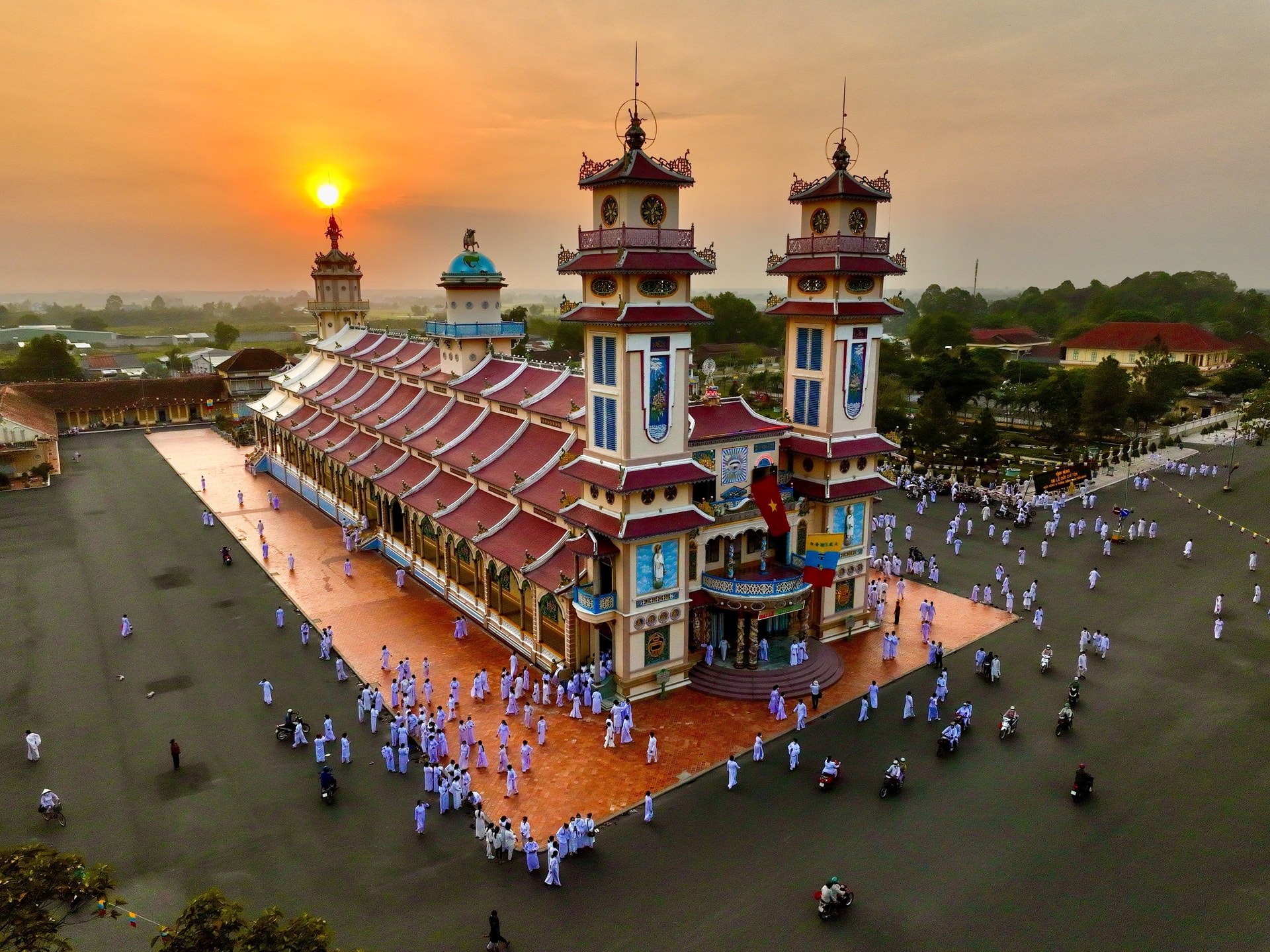 Sunset view of Cao Dai Temple in Tay Ninh, with worshippers dressed in traditional white robes gathered around the colorful temple