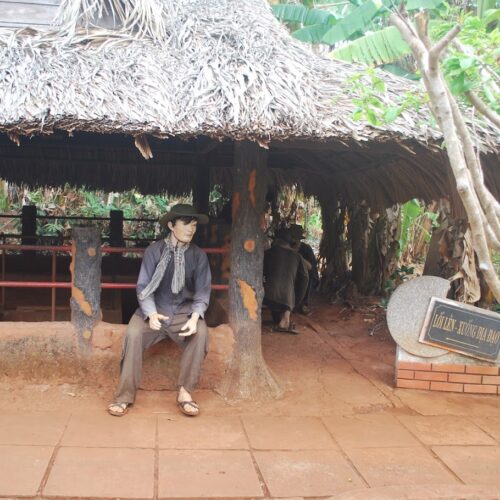 Vietnamese soldier statue sitting in front of a thatched hut with an underground tunnel entrance, part of the Long Tan – Long Phuoc Tunnels historical site.