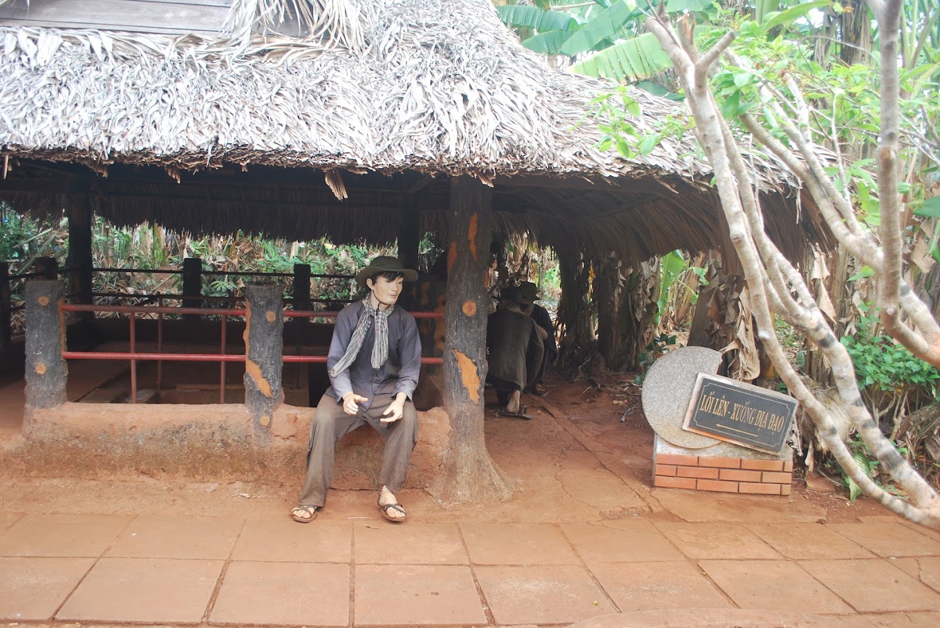 Vietnamese soldier statue sitting in front of a thatched hut with an underground tunnel entrance, part of the Long Tan – Long Phuoc Tunnels historical site.