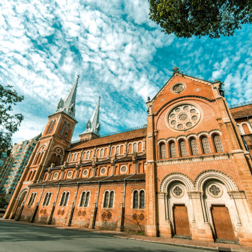 Side view of Saigon Notre-Dame Cathedral Basilica under a bright blue sky in Ho Chi Minh City.