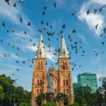 Front view of Saigon Notre-Dame Cathedral with flocks of pigeons flying across the square.