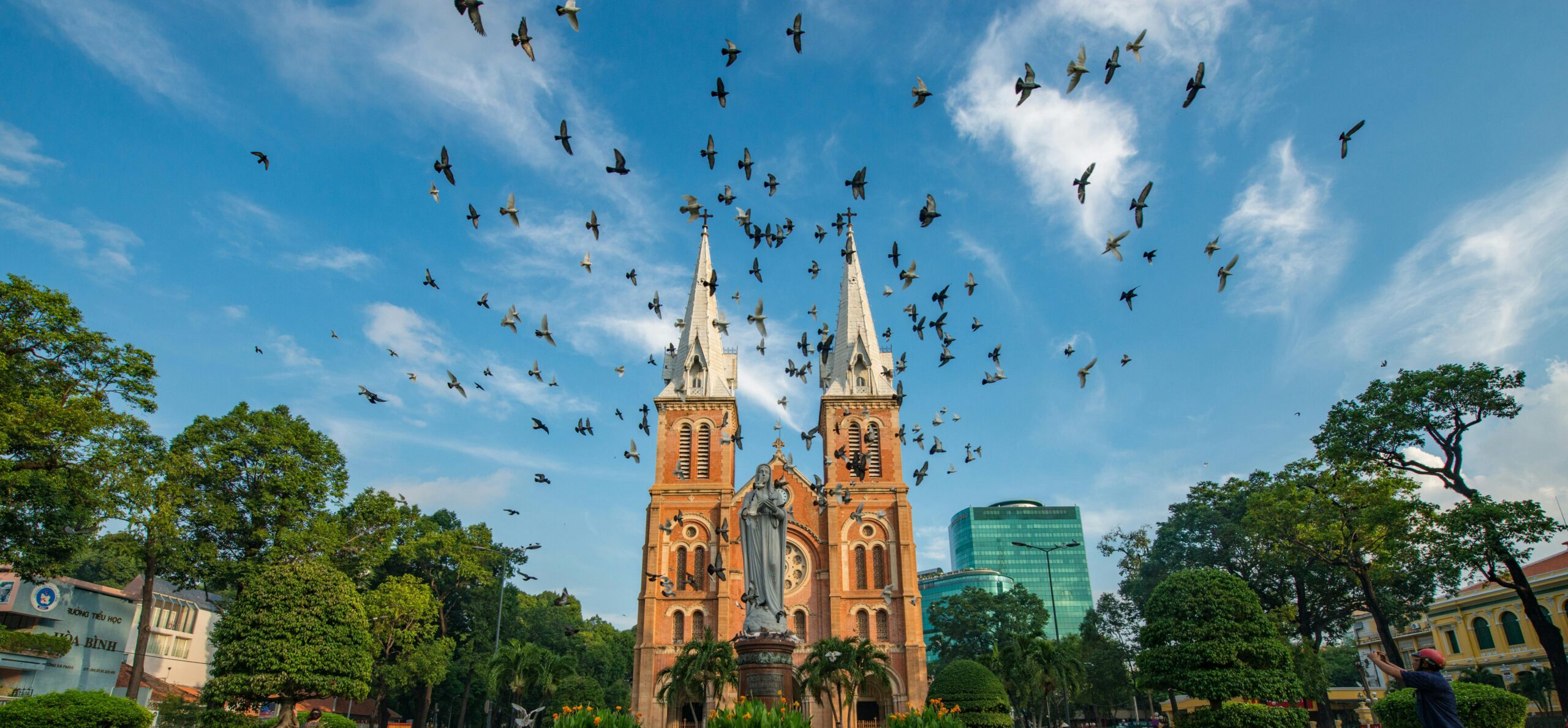 Front view of Saigon Notre-Dame Cathedral with flocks of pigeons flying across the square.