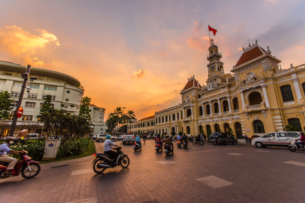 Saigon Opera House at sunset with motorbikes passing by in Ho Chi Minh City.