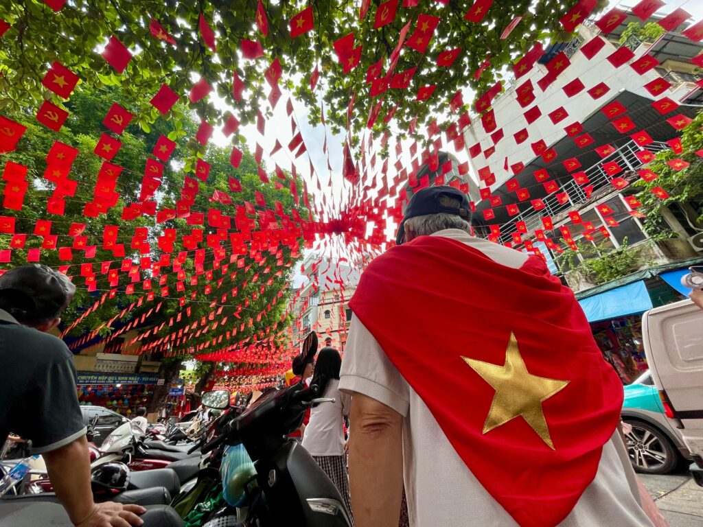 People draped in Vietnamese flags on a street decorated in vibrant red national colors