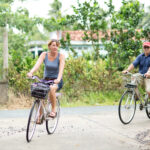 Two tourists are cycling through a country road in mekong delta