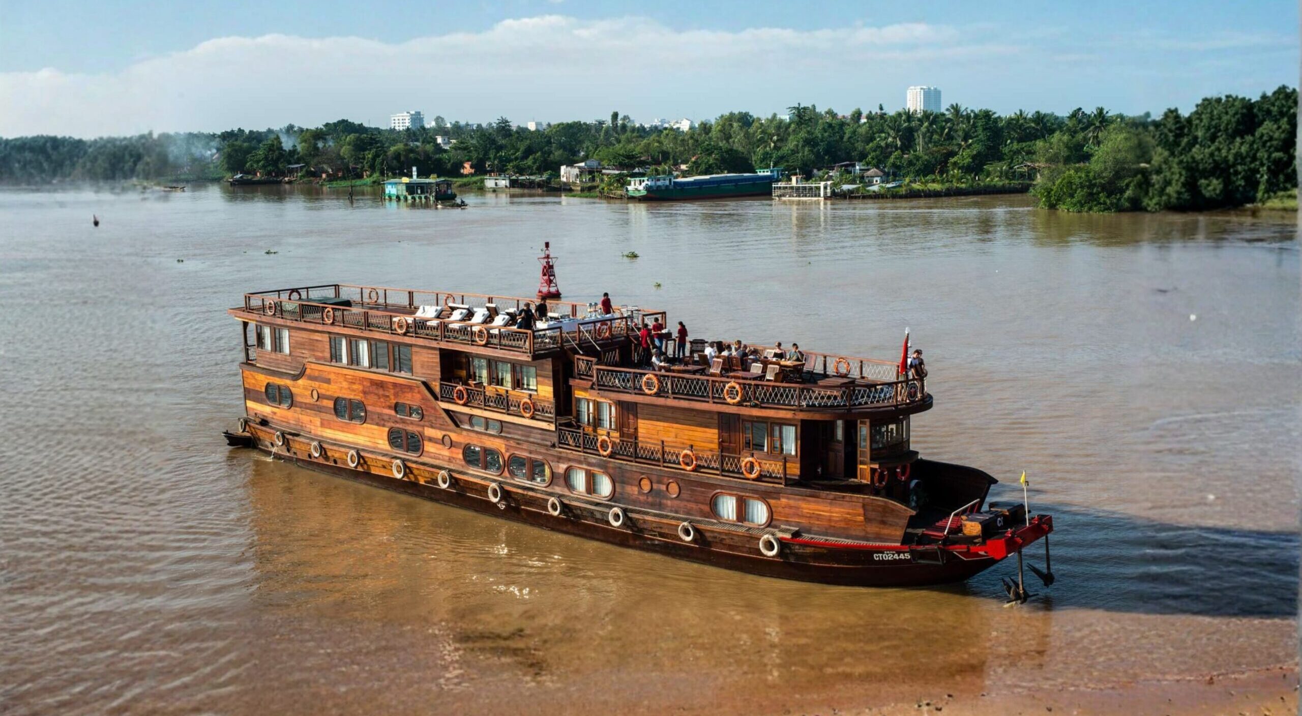 Large wooden cruise boat sailing through lush green riverbanks of the Mekong Delta.