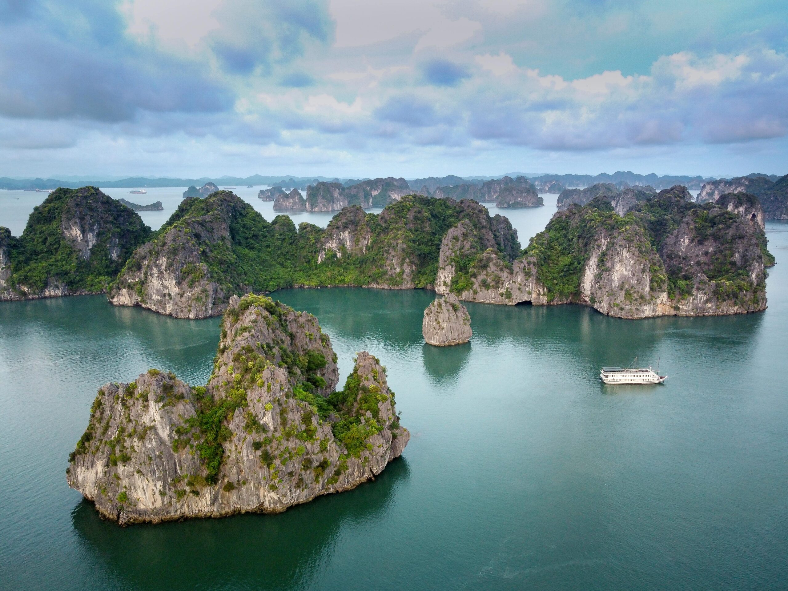 Panoramic view of Ha Long Bay from above, with a cruise ship passing by the limestone rocks