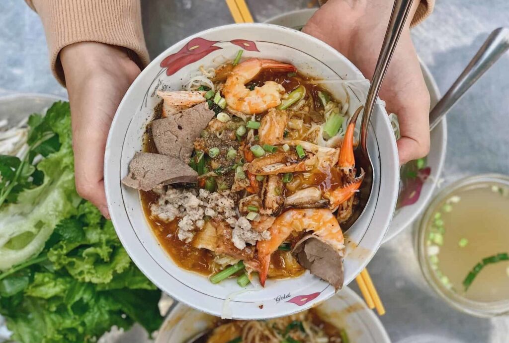 Bowl of Hu Tieu noodle soup with shrimp, crab, pork, and liver toppings.
