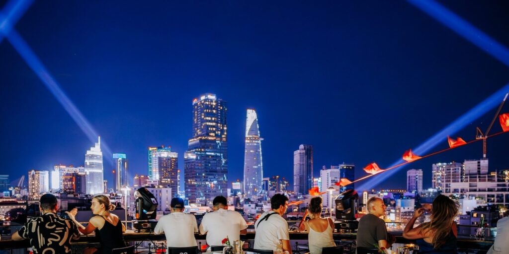 Group of people enjoying cocktails at a rooftop bar with night views of Ho Chi Minh City