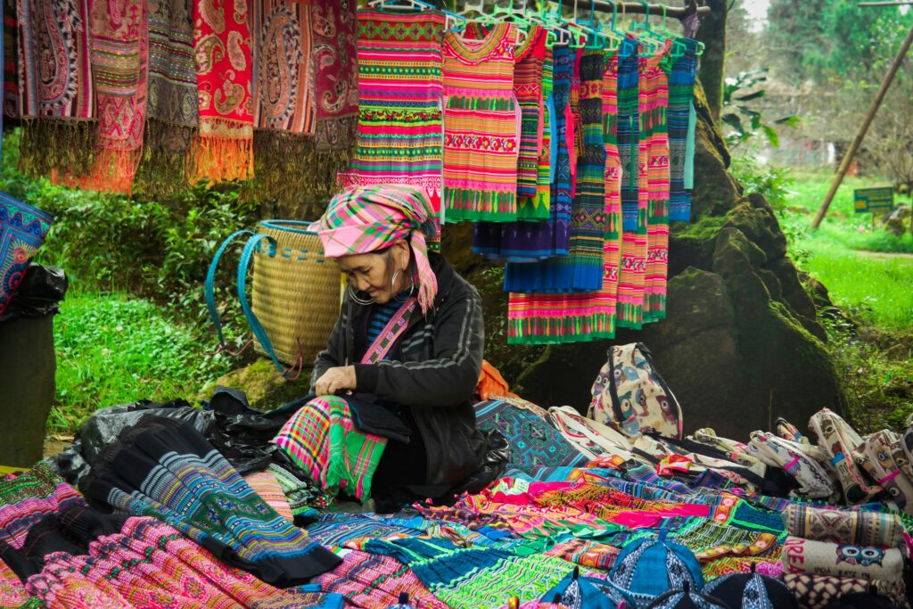 An elderly woman of the Hmong ethnic group is sitting selling fabric with traditional patterns of her people.