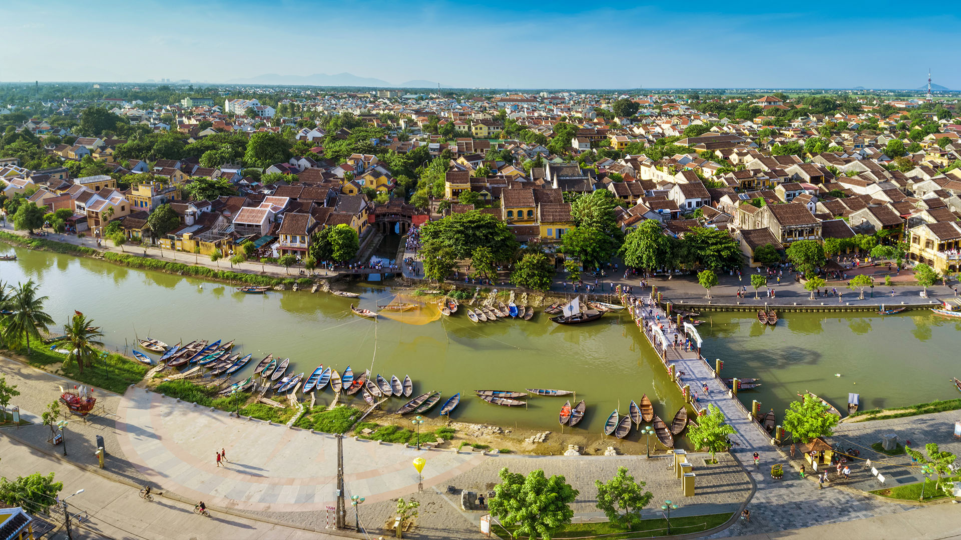 High-angle view of Hoi An Ancient Town, showcasing traditional yellow houses and wooden boats floating along the river. Capturing one of the Central Vietnam Highlights