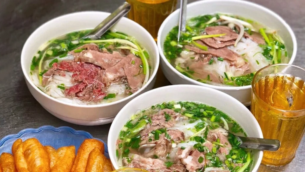 Three bowls of Hanoi-style pho bo served with fried dough sticks (quay) and iced tea