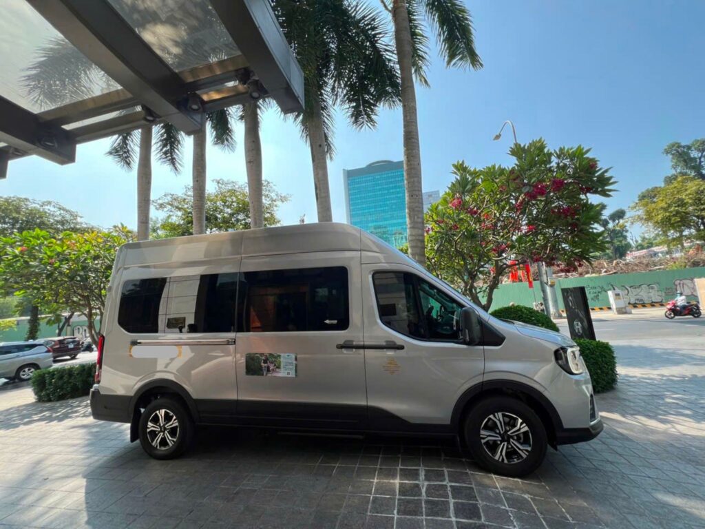 A white 16-seater van is parked in front of the hotel to pick up tourists for the Ginkgo Voyage.